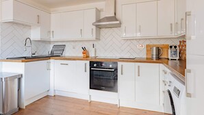 Une cuisine moderne avec des armoires blanches, une hotte de cuisinière en acier inoxydable et un four Bosch.