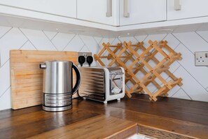 A kitchen with white cabinets, a wooden cutting board, a stainless steel kettle, a vintage toaster, and a wooden wine rack. - Contemporary 2BD Flat with Balcony, Shoreditch (Greater London)