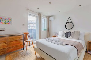 A bedroom with a bed, a wooden dresser, a chair, a window, and an air conditioning unit. - Contemporary 2BD Flat with Balcony, Shoreditch (Greater London)