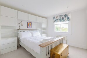 A bedroom with a bed, bedside tables, a radiator, a window with a curtain, and built-in shelving.