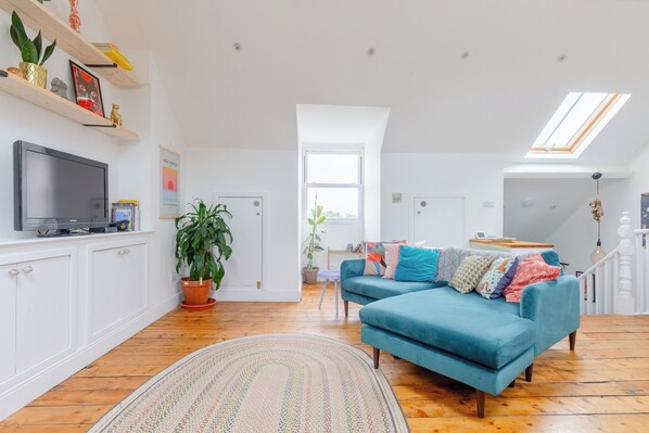 A modern living room with a blue sofa, wooden flooring, and a skylight.