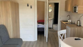 Quarto compacto com cama, pequena cozinha, área de refeições com mesa e cadeiras e sofá cinza.
