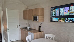 Een compacte keuken met een magnetron, spoelbak en een kleine koffiezetapparaat. Er staat een witte eettafel met vier stoelen.