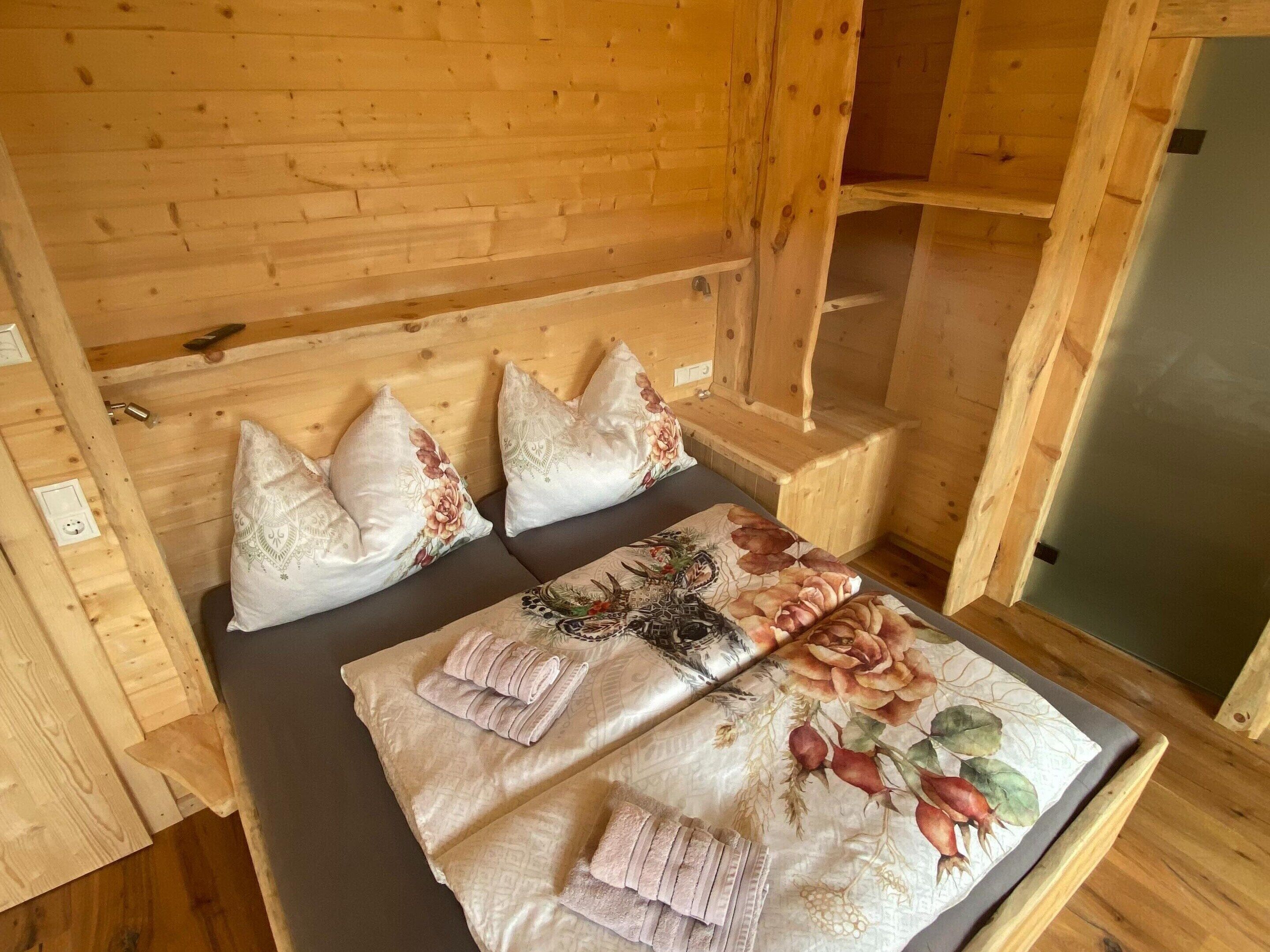 A wooden cabin interior with a bed, pillows, and a window.