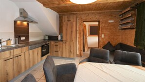 Eine kleine Küche mit modernen Geräten, ein Essbereich mit Tisch und Stühlen sowie eine Holzbalkendecke.
