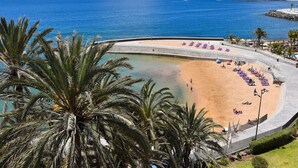 Una passeggiata lungomare con spiaggia sabbiosa, palme e mare cristallino.