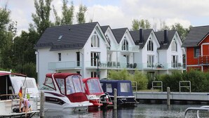 Filas de casas blancas con techos oscuros, un muelle con barcos y una masa de agua tranquila.