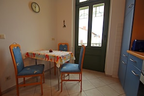 A kitchen with a dining table, chairs, cabinets, a clock, and a window with a view. - Ferienwohnung Meeresrausch in Ahlbeck (Heringsdorf)