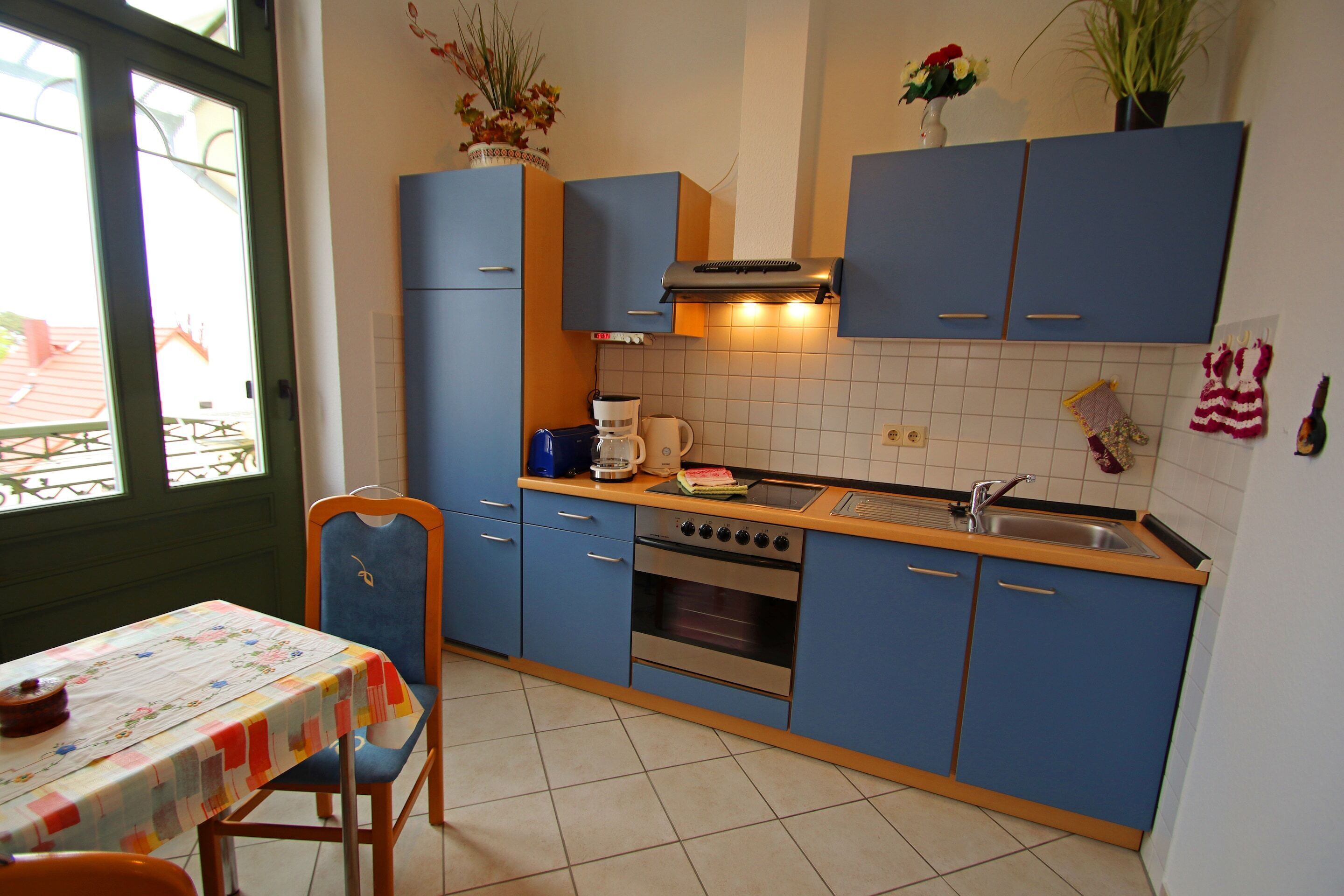 A kitchen with blue cabinets, a stove, a sink, and a table with a floral tablecloth.