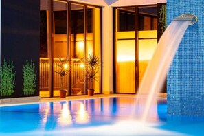 Un espace piscine agrémenté d’une cascade, d’un éclairage intérieur et de plantes en pot.
