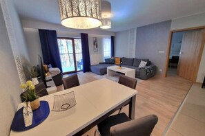 A modern living room with a sofa, a dining table with chairs, and a large window with curtains. - Holiday Apartment, Sauna, Pool, Szklarska Poreba (Szklarska Poreba)