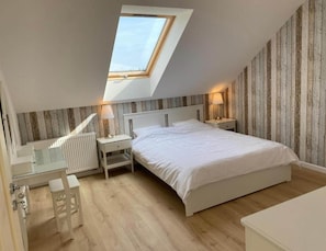 A bedroom with a skylight, wooden panel walls, a white bed, bedside tables with lamps, and a small stool. - Holiday House for 5 People in Grzybowo (Kolobrzeg)
