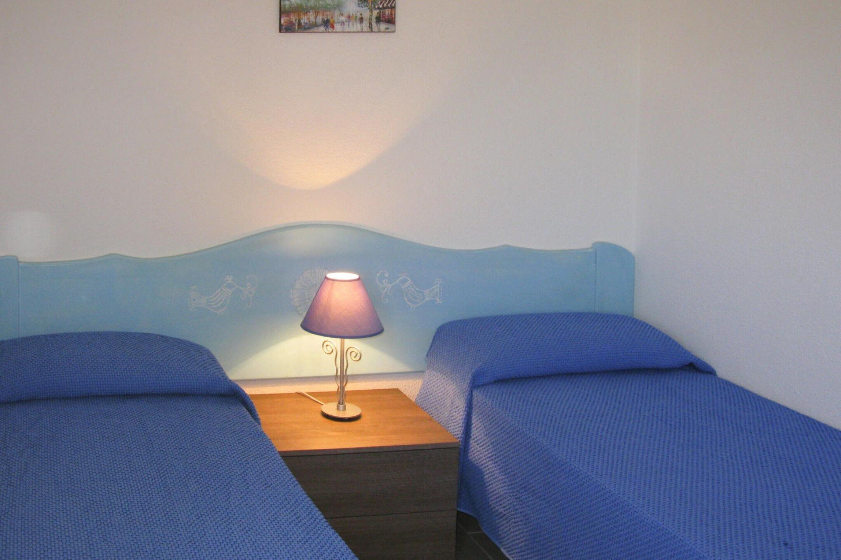 A room with two single beds, a nightstand with a lamp, and a wall with a picture.