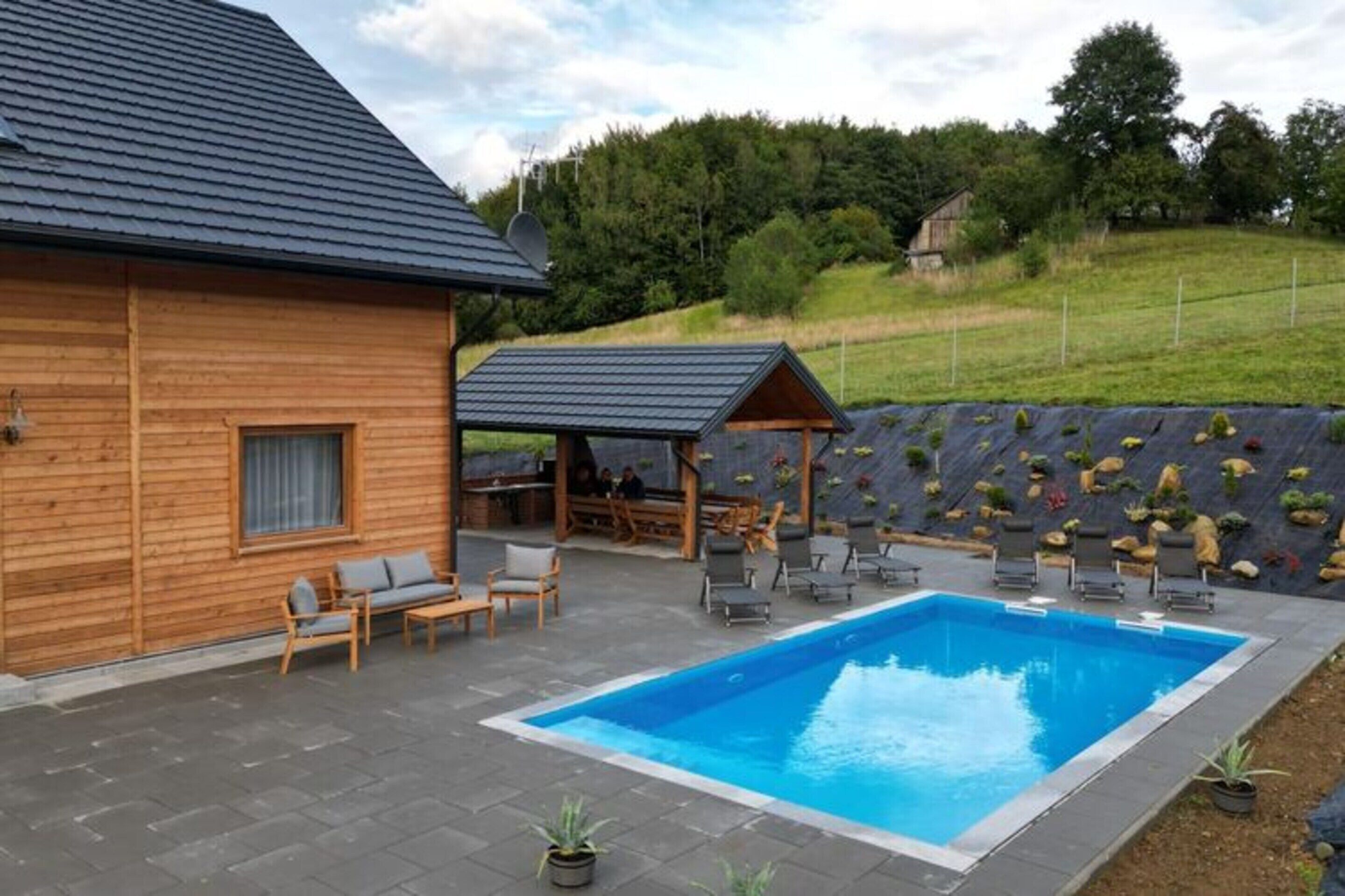 A wooden cabin with a swimming pool, outdoor seating, and a rock garden.