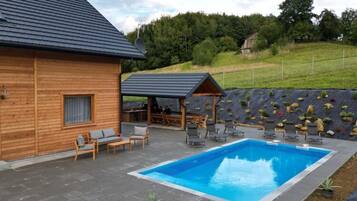 A wooden cabin with a swimming pool, outdoor seating, and a rock garden.