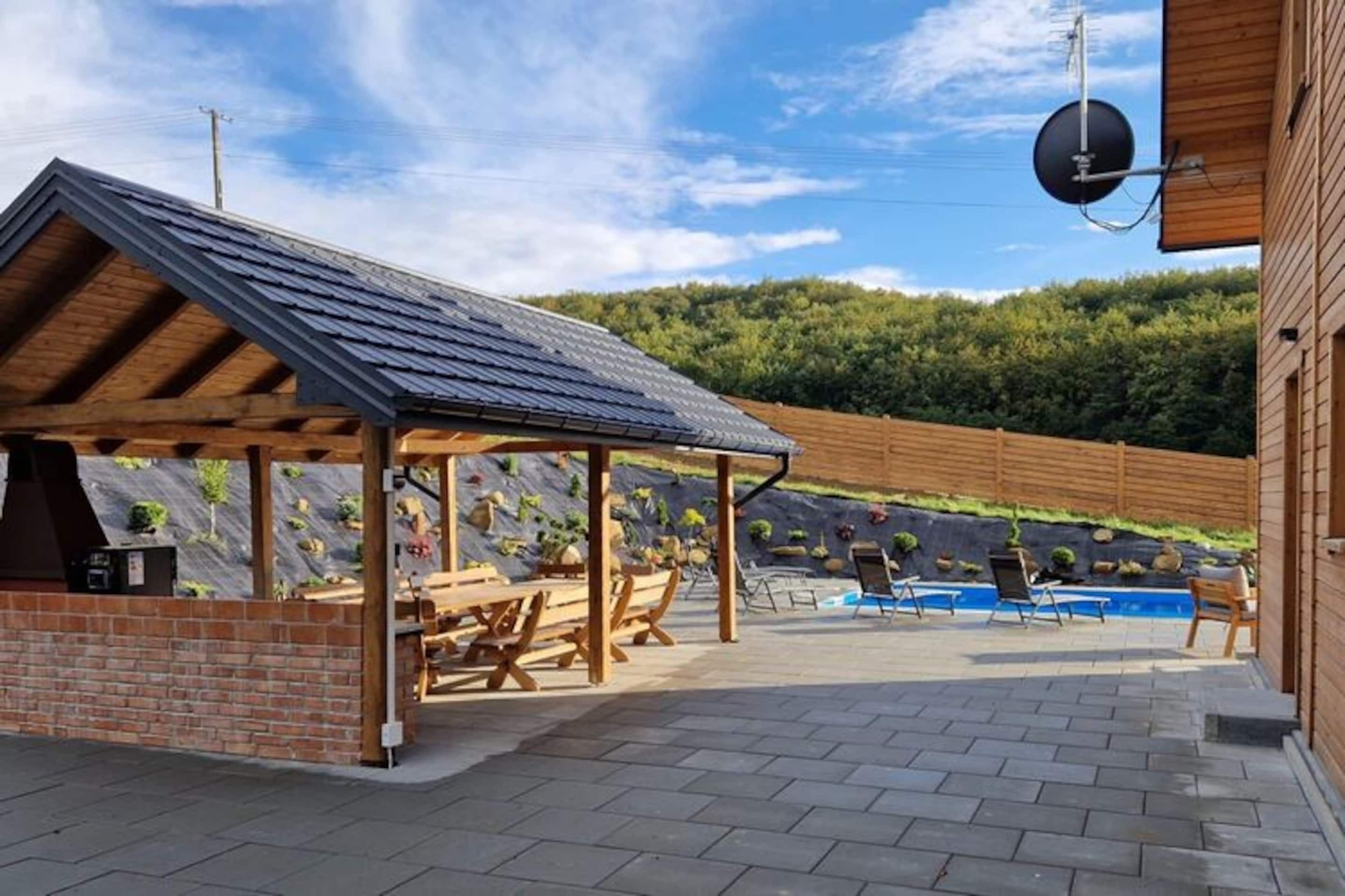 A covered outdoor area with a barbecue station, pool, and lounge chairs.