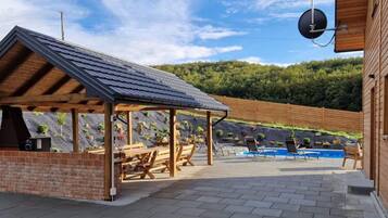 A covered outdoor area with a barbecue station, pool, and lounge chairs.