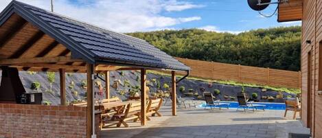 A covered outdoor area with a barbecue station, pool, and lounge chairs.