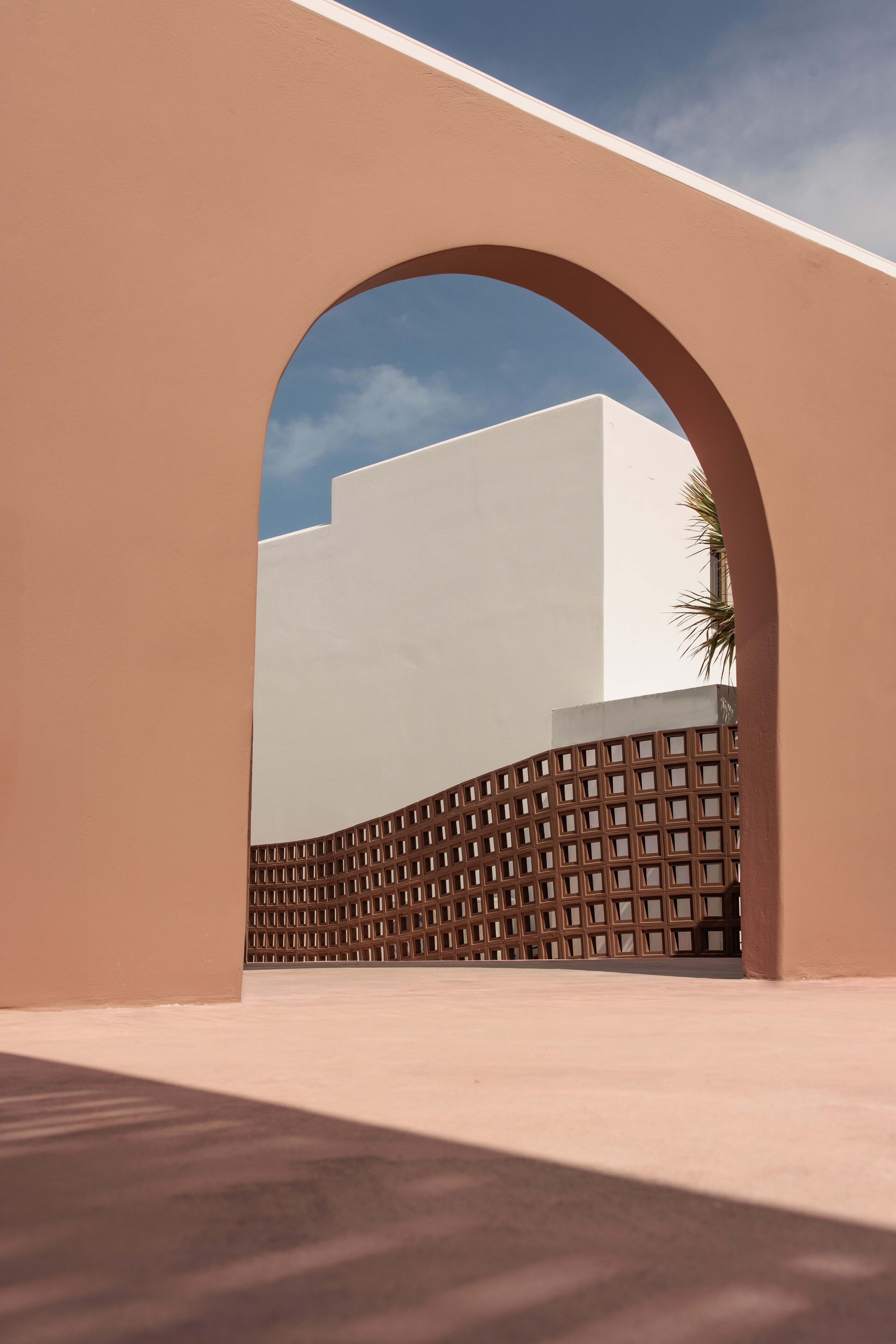 Una estructura arquitectónica con un gran arco, un edificio de techo plano y una cerca con celosías.