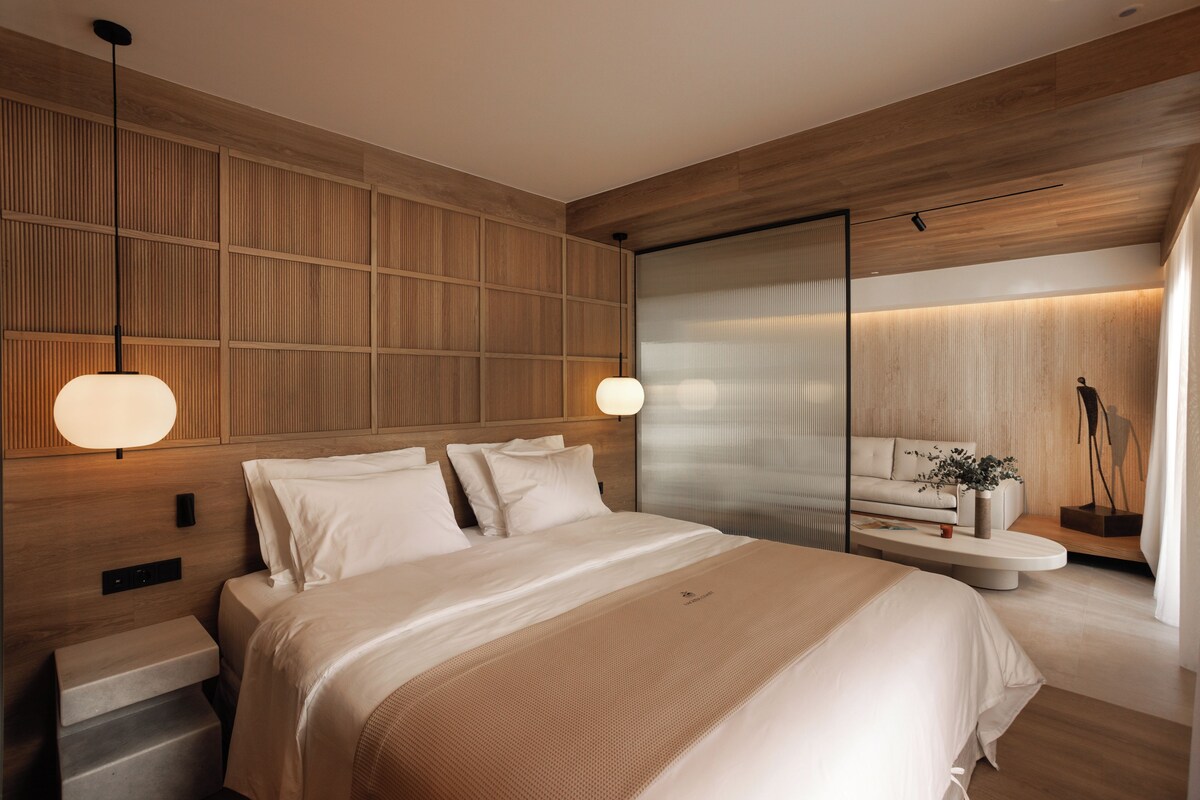 Una camera d'albergo moderna con un letto grande, comodini, una poltrona e un tavolino con una pianta.