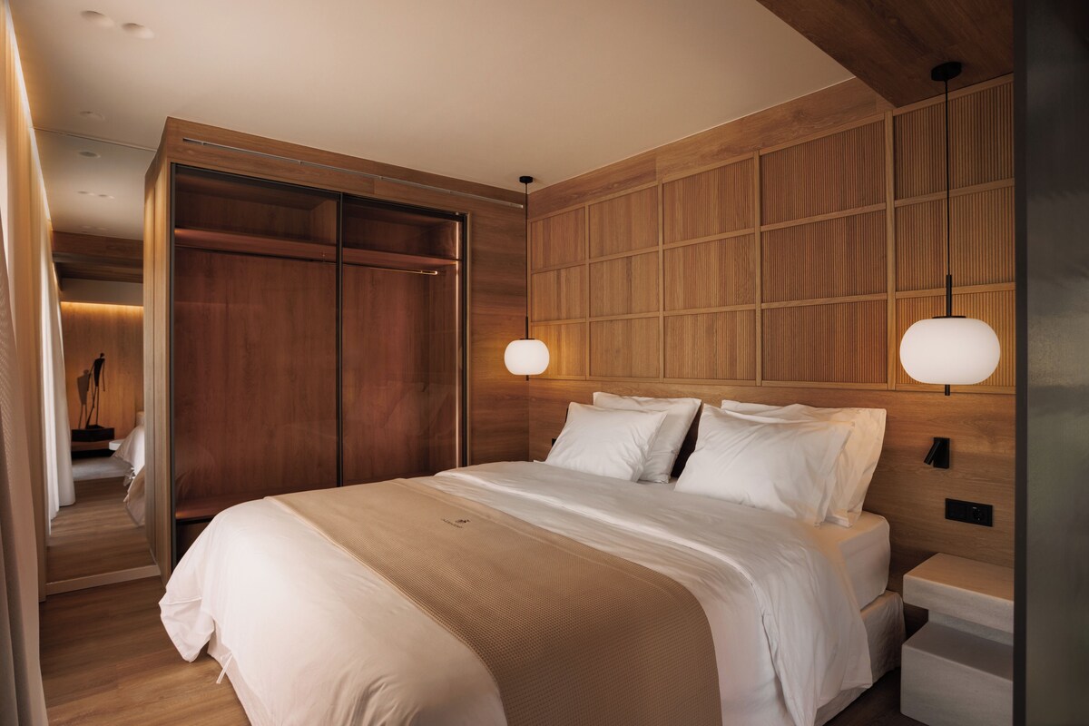 A modern hotel room with a large bed, wooden paneling on the walls, and a walk-in closet.