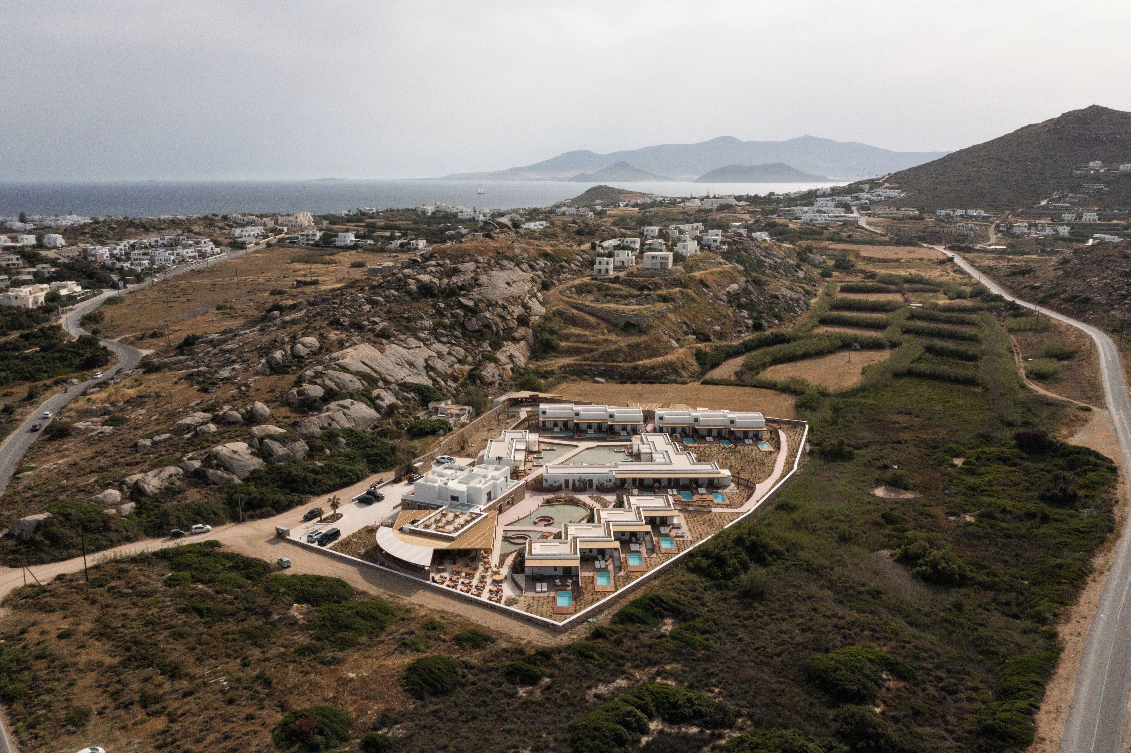 An aerial view of a resort with multiple buildings, a winding road, and a mountainous backdrop.