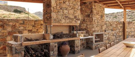 An outdoor kitchen with stone walls, a brick fireplace, and a long dining table.