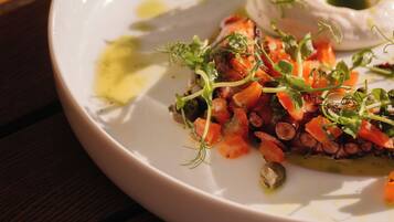 A white plate with a dish of octopus, carrots, and greens, served on a wooden table.