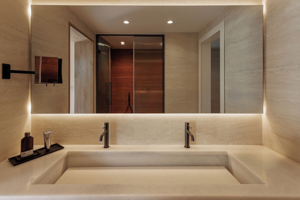 Un baño moderno con una bañera rectangular grande, dos grifos empotrados en la pared y un espejo sobre la bañera.