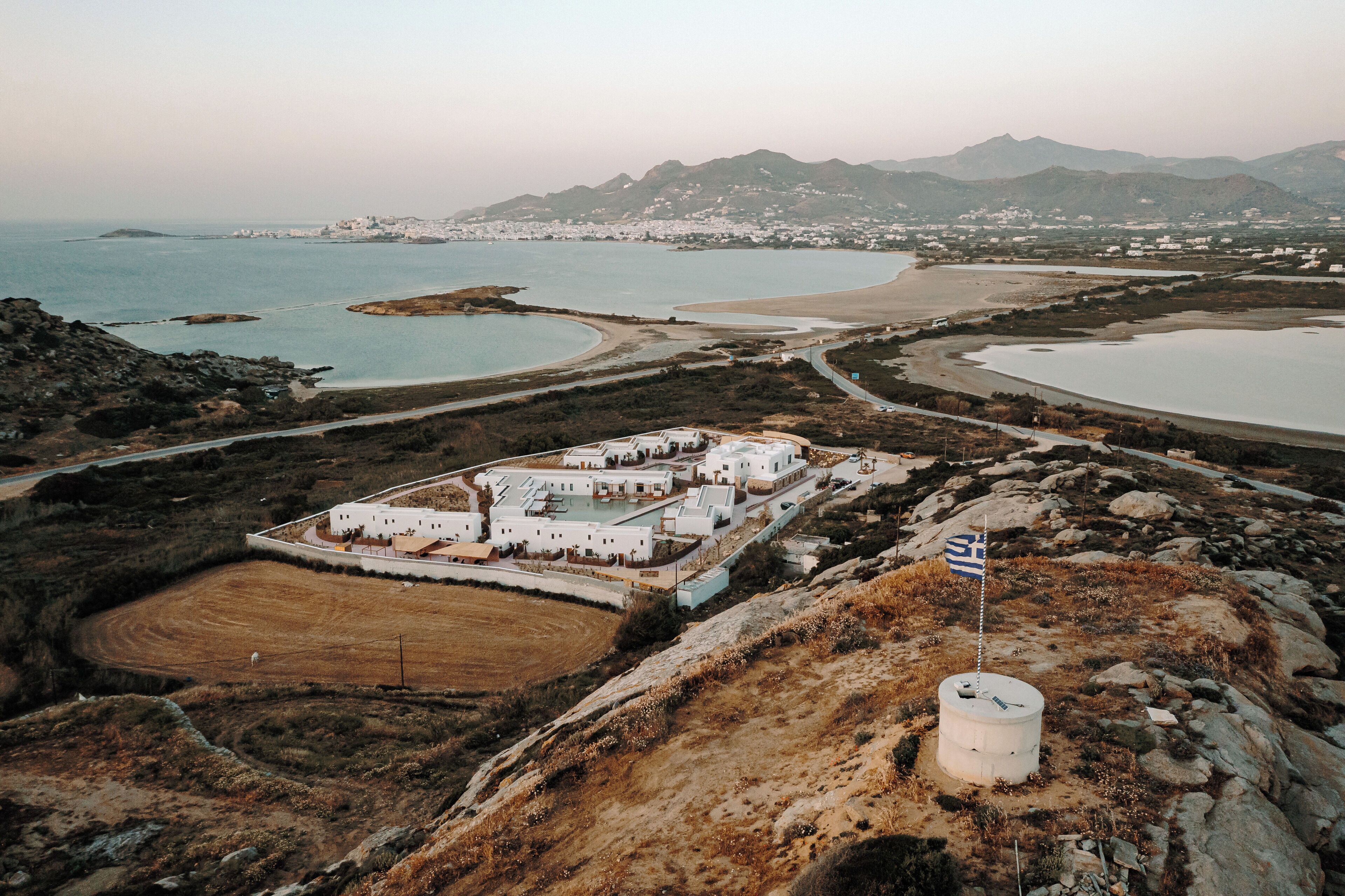 An aerial view of a coastal resort with multiple buildings, a large sandy beach, and a rocky terrain.