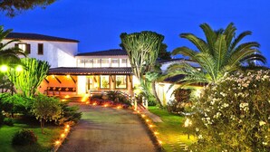 A well-lit residential property with a paved driveway, a large cactus, and various flowering plants. - Residence Cormoran, Loc. Campus Villasimius (Villasimius)
