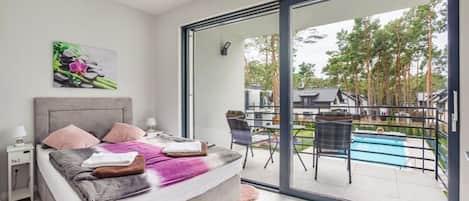 A bedroom with a bed, a nightstand, a painting, and a view of a swimming pool and outdoor seating area.