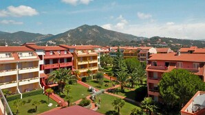 Un hotel con varios edificios de techo rojo, dispuestos en un patio con palmeras y una montaña al fondo.