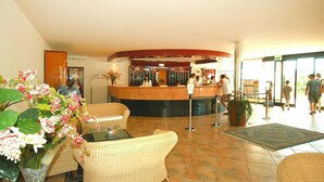Un hall con mobiliario de mimbre, una mesa de recepción y un ventanal grande.