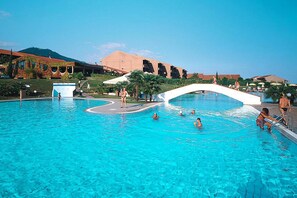 A large outdoor swimming pool with a white bridge, palm trees, and buildings in the background. - Nice Apartment in Loano With Shared Pool (Loano)