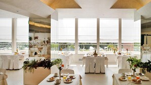 Un comedor moderno con amplios ventanales, decoración en blanco y mesas ordenadas.