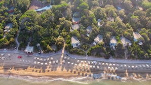 Luchtbeeld van een kustgebied met strandparasols, een weg en gebouwen met traditionele daken.
