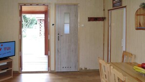Ein Zimmer mit Holzboden, einem Esstisch mit Stühlen, einem Fernseher auf einem Schrank und einer Tür, die nach draußen führt.