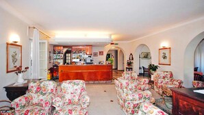 A hotel lobby with floral-patterned armchairs, a reception desk, and a bar area. - Apartment in Mongelia (Moneglia)