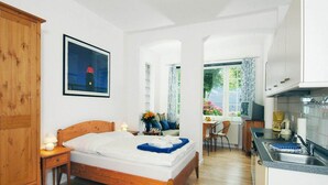 A bedroom with a wooden bed, a nightstand, a desk, and a window with curtains. - Ferienwohnung, Wyk auf Fohr (Wyk auf Foehr)