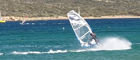 A person windsurfing on a clear day with a hilly landscape in the background.