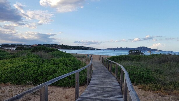 A wooden boardwalk leading to a beach with a view of the sea and distant hills. - Apartment in Porto Pollo Near Surf Paradise (Palau)