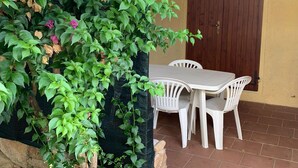 A patio with a table and chairs, a wooden door, and a wall covered with green foliage. - Apartment in Porto Pollo Near Surf Paradise (Palau)