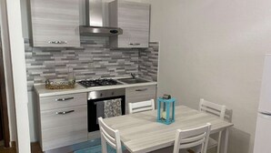 A compact kitchen with a gas stove, sink, and a small dishwasher. There is a dining table with chairs and a blue rug on the floor. - Apartment in Porto Pollo Near Surf Paradise (Palau)