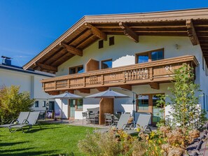 A two-story building with a wooden balcony, outdoor seating area, and a well-maintained lawn. - Apartment in Brixen Near Wilder Kaiser Gondola (Brixen im Thale)