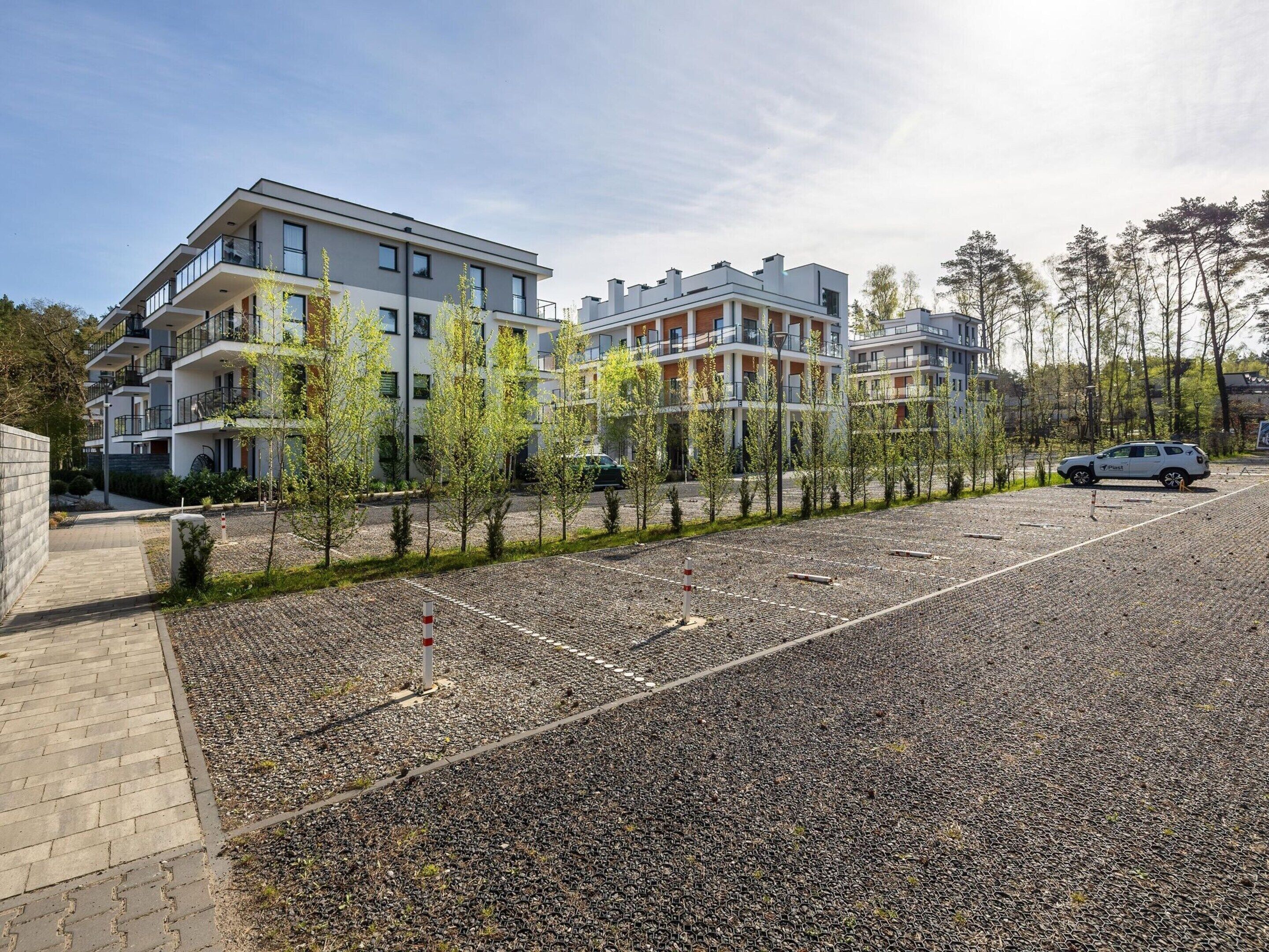 Un complejo de apartamentos moderno con varios edificios, un estacionamiento de grava y árboles jóvenes.