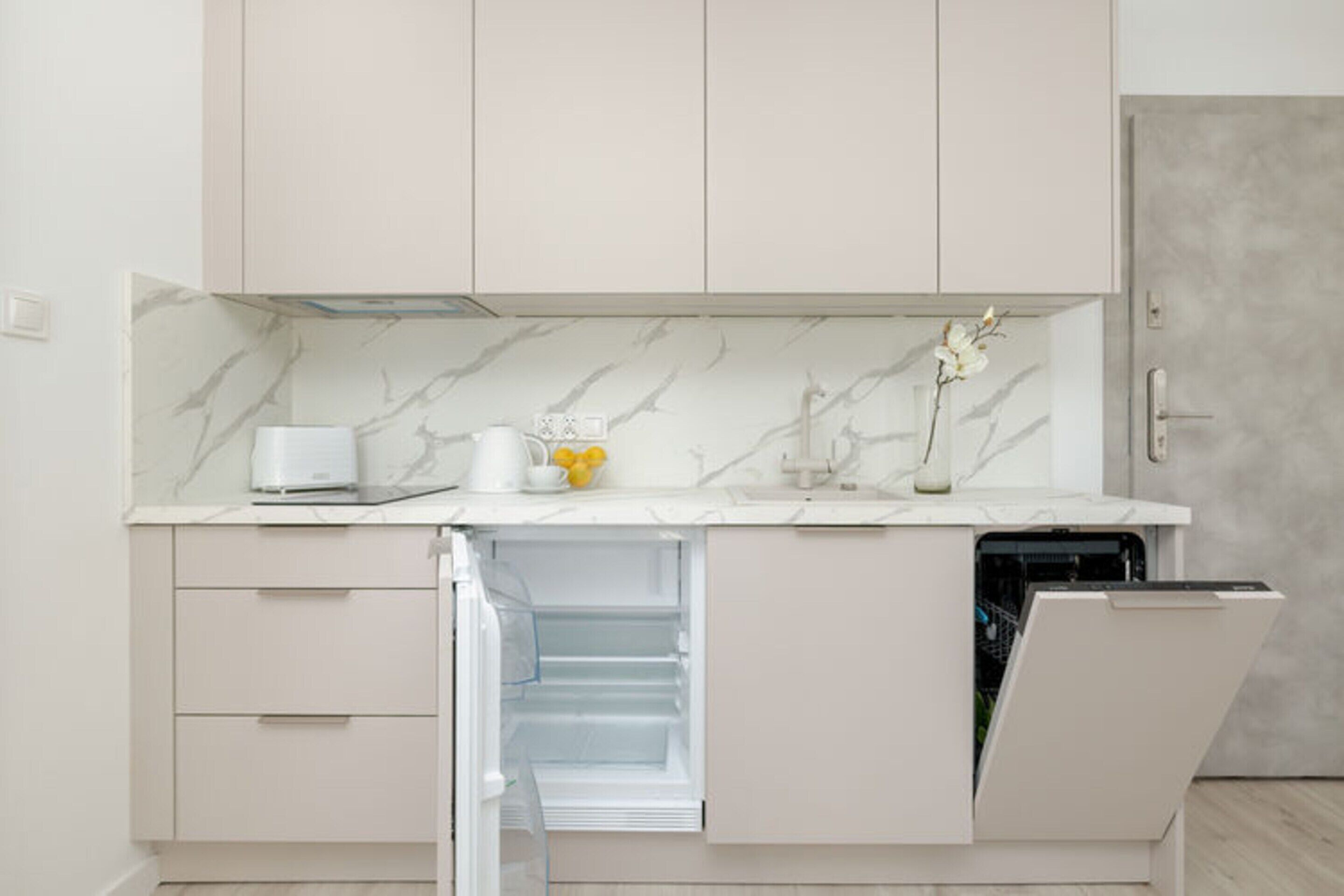 A modern kitchen with a built-in dishwasher, a marble backsplash, and a white countertop.