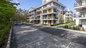 Ein modernes Apartmenthaus mit mehreren Balkonen, einer gepflasterten Auffahrt und umliegender Bepflanzung.