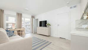 Ein modernes, helles Wohnzimmer mit einer Couch, einem Fernseher, einem Essbereich und einer Küchenzeile.