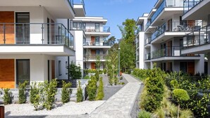 Ein modernes Wohngebäude mit mehreren Balkonen, einem zentralen Innenhof mit Pflanzen und blauem Himmel.